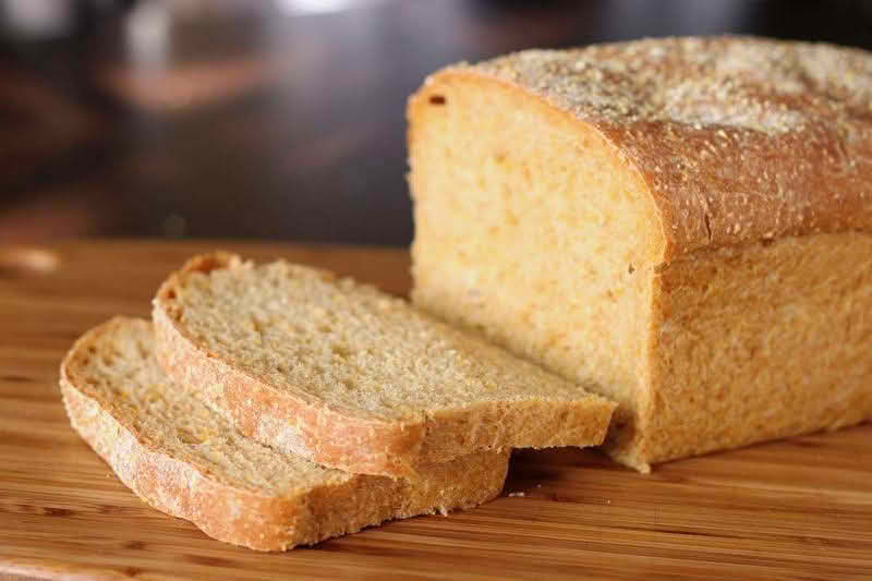 A loaf of anadama bread resting on a wooden cutting board, showcasing its rustic texture and golden-brown crust