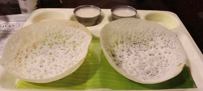 Two Appam pancakes served with coconut milk arranged neatly on a tray
