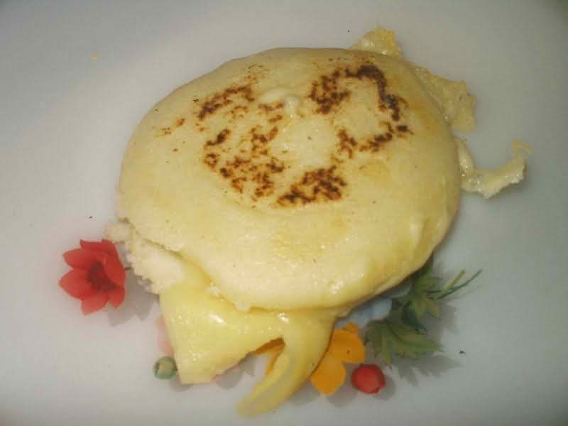 A plate featuring a golden arepa, a traditional cornmeal dish, with a cheese filling, garnished and ready to be enjoyed