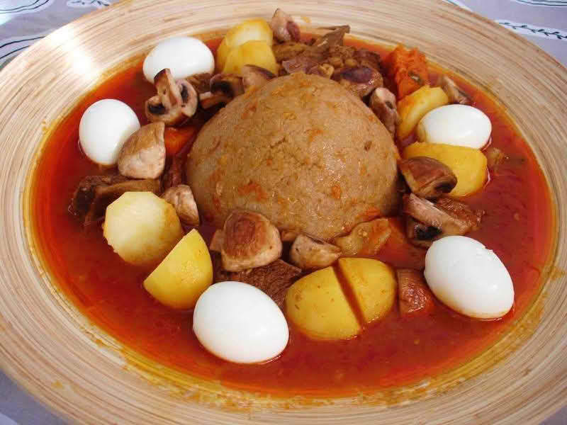 A plate of Bazin (center) served with a stew and whole hard-boiled eggs