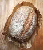 A loaf of bread resting on a rustic wooden table, showcasing its golden crust and inviting texture