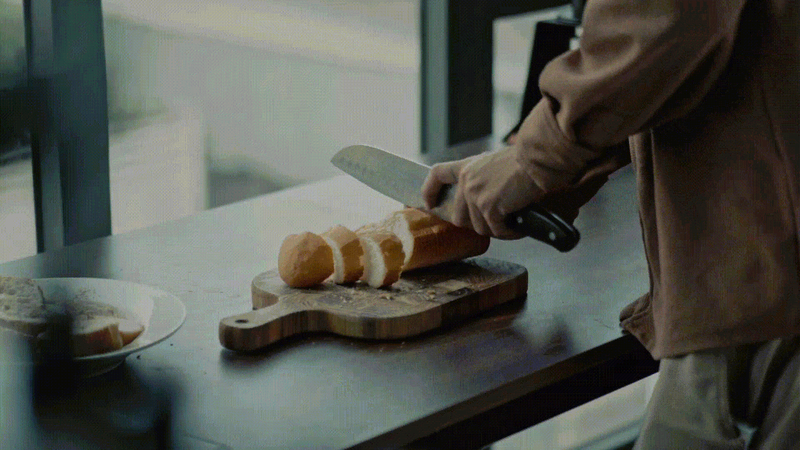Close-up short looping video of someone slicing a baguette on a bread board